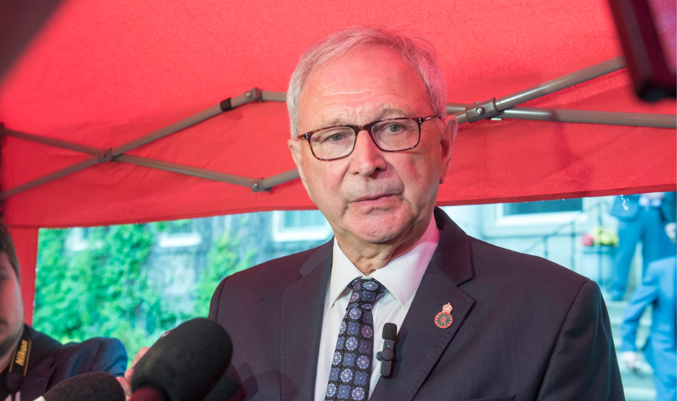 Blaine Higgs seen head and shoulders under a red tent outdoors speaking to reporters