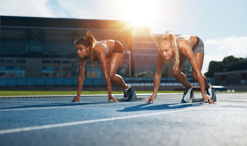 Two female athletes crouched at the start line of a running track