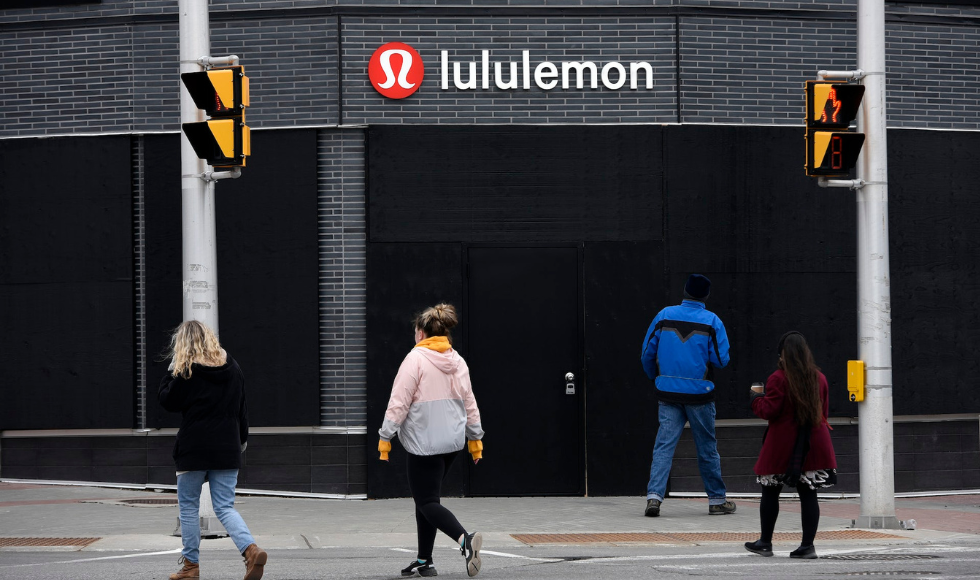 pedestrians seen from behind walking in front of a building with a Lululemon sign on it.