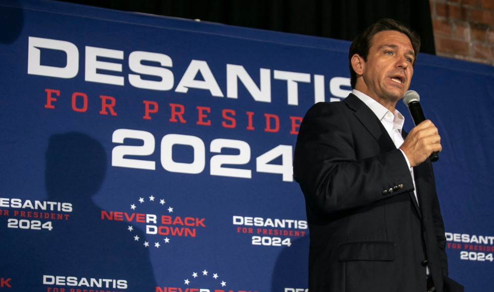 Ron DeSantis holding a mic in front of a banner with his name