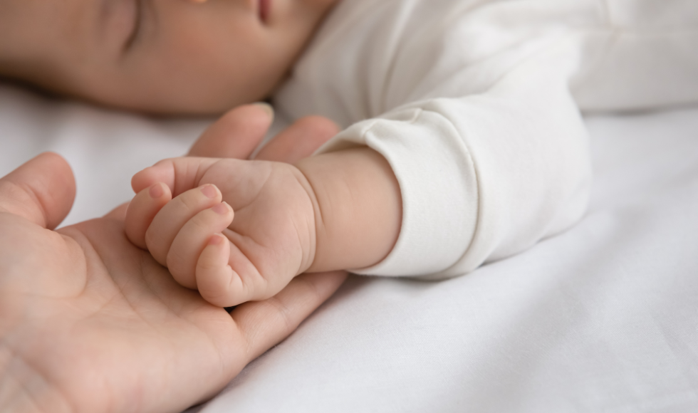 A sleeping baby's hand resting on an adult hand