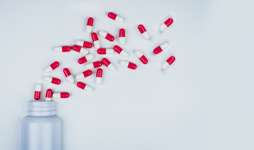 An unlabelled pill bottle on its side with red and white pills falling out