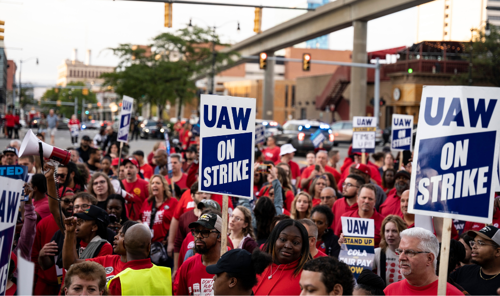 Striking workers hold up picket signs that say UAW on strike