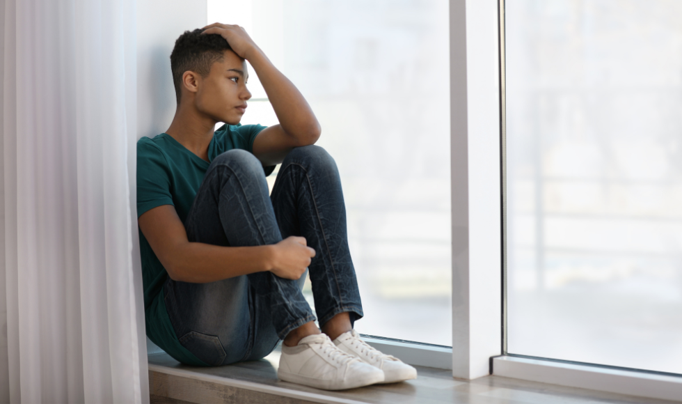 A Black youth sitting looking out a window
