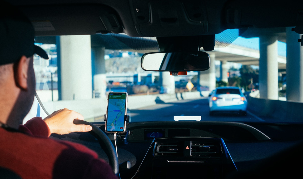 Scene from the back seat, a driver in traffic with a ride app on his dash-mounted phone.