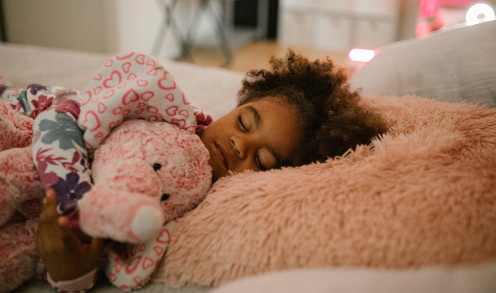 A young girls holds a stuffed elephant as she sleeps in her bed.