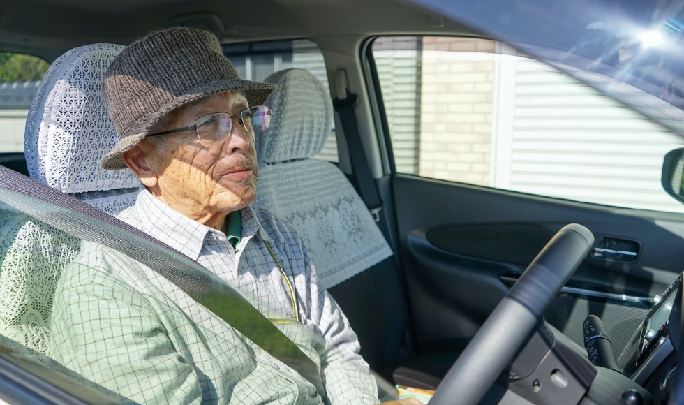 An older individual sitting at the wheel of a car.
