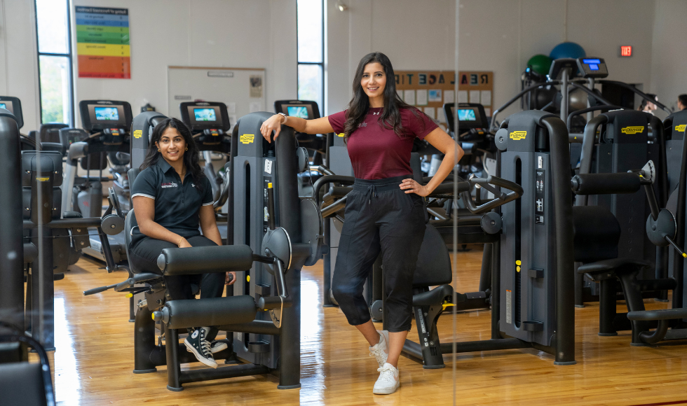 Two smiling women in a gym surrounded by fitness equipment