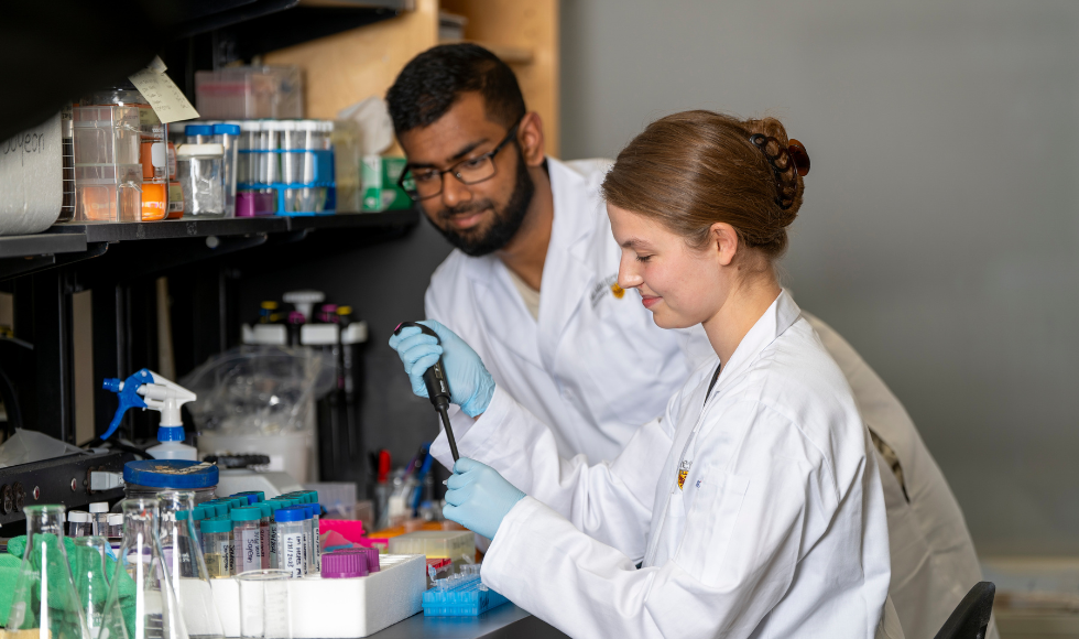 Two student researchers in lab coats working in a lab