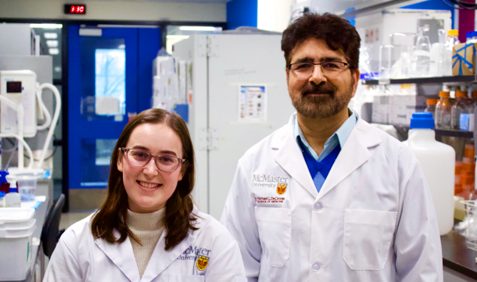Two researchers wearing white lab coats smiling at the camera