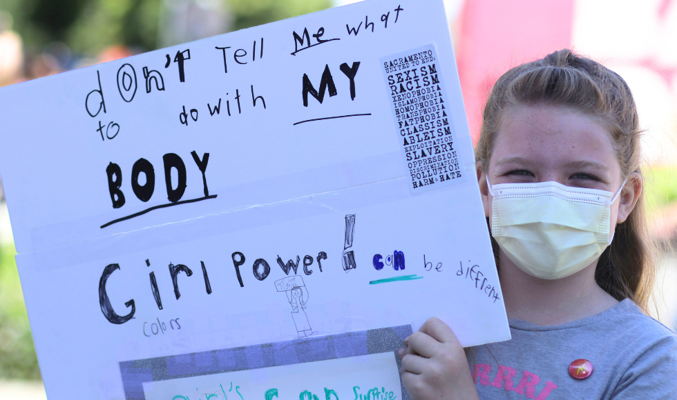 A girl holding a sign that says don't tell me what to do with my body