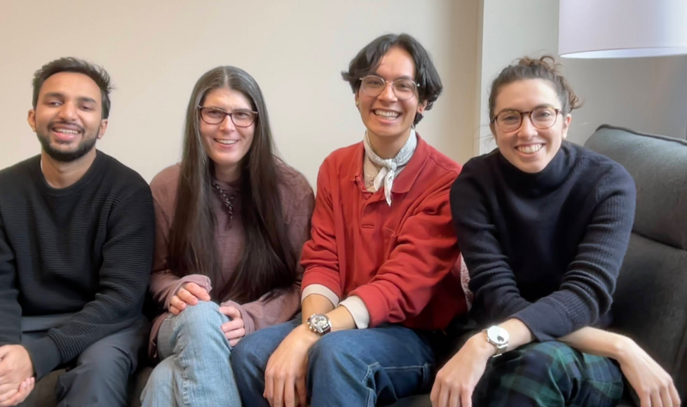 Image of Graduate students Shreshth Saxena, Maya Flannery and Joshua Schlichting sitting on a couch smiling for a photo with professor Lauren Fink
