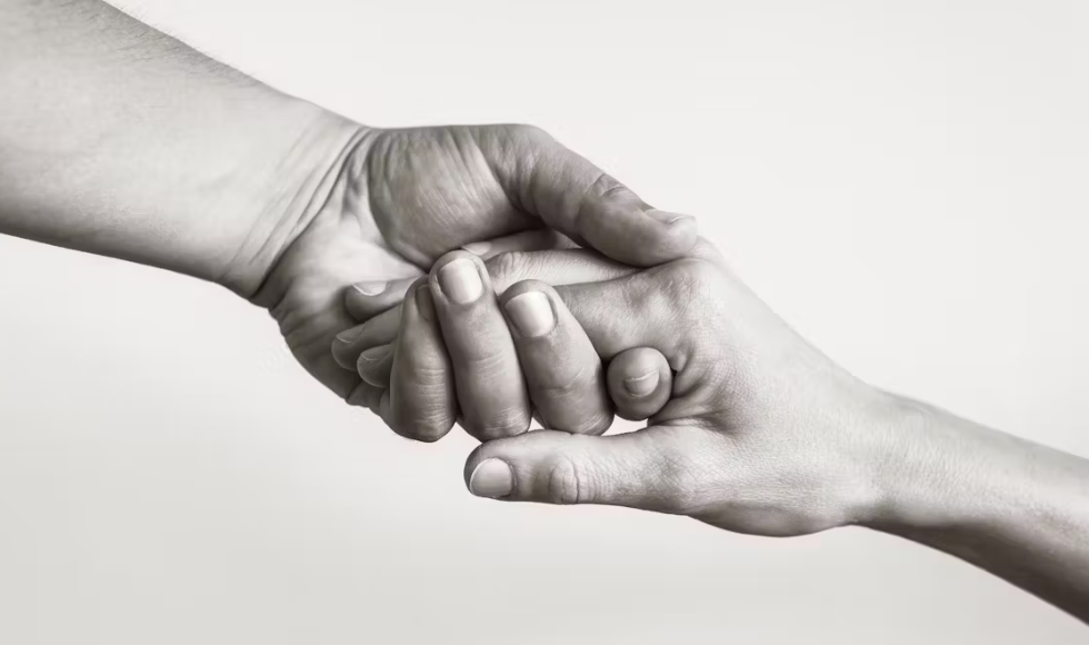 Black and white image of two hands reaching out and holding onto one another