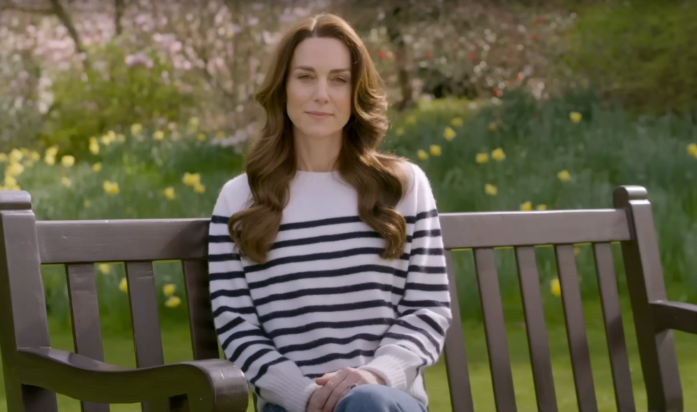 A screenshot from the beginning of the Princess of Wales video statement showing her sitting on a bench outside wearing a striped sweater and jeans.