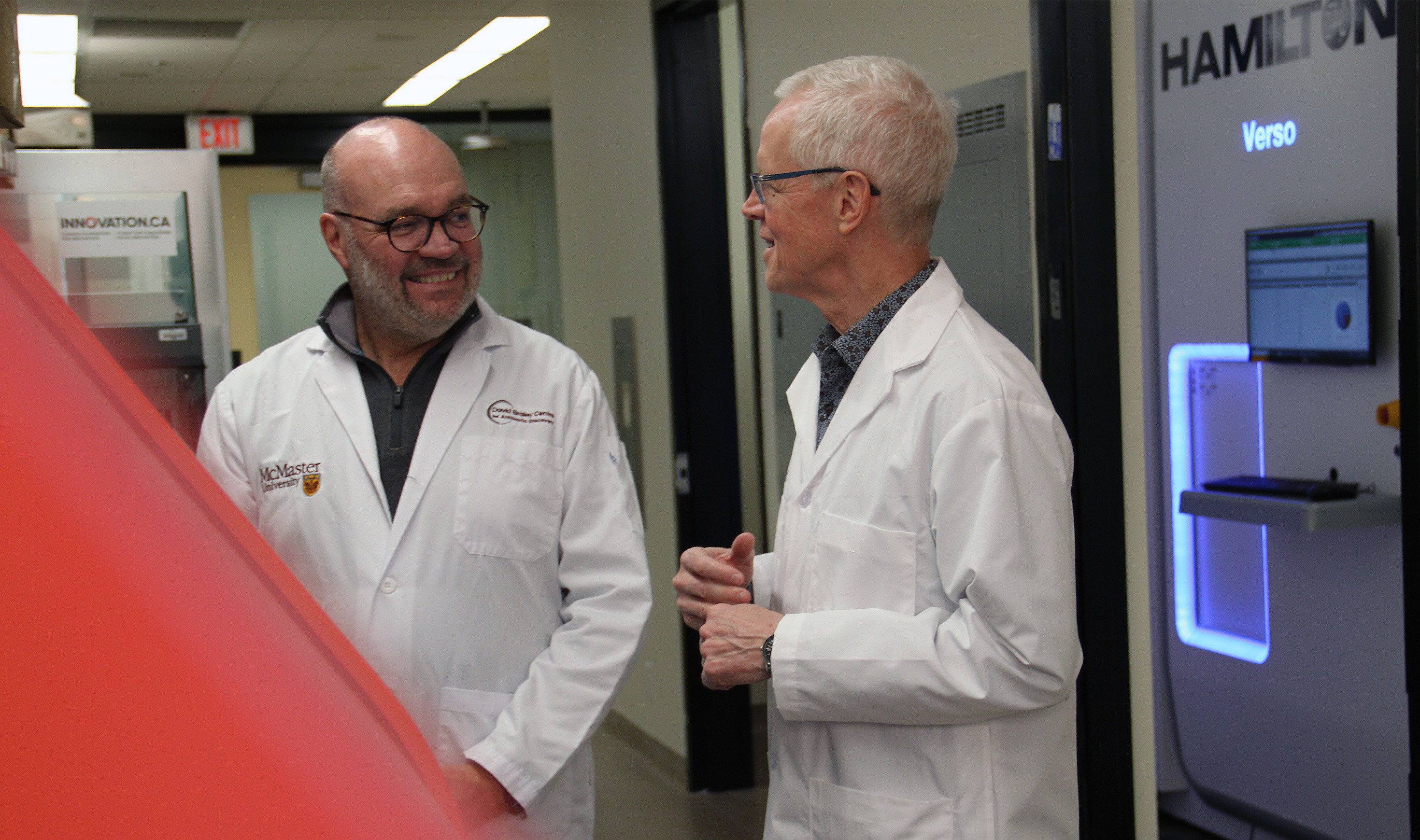 Gerry Wright and Eric Brown, wearing lab coats in a lab, smile at each other.