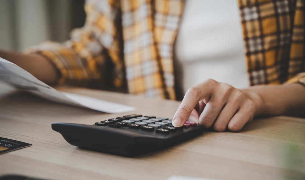 closeup of a person's hands on a calculator while their other hand holds paper.