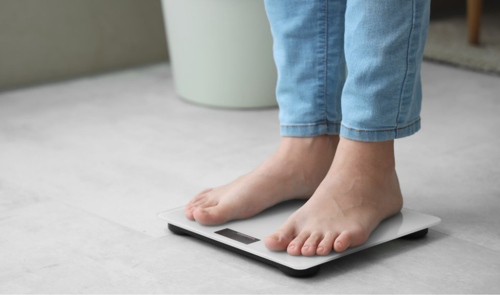 Feet and lower legs of a person in jeans standing on a scale.