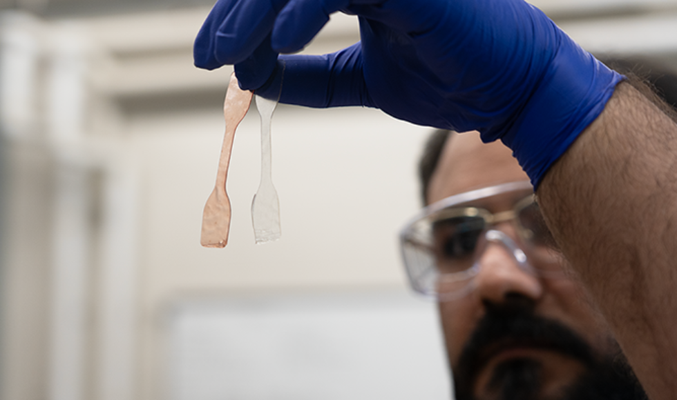 A tight shot of a test strips being held up by a person wearing medical gloves and goggles.