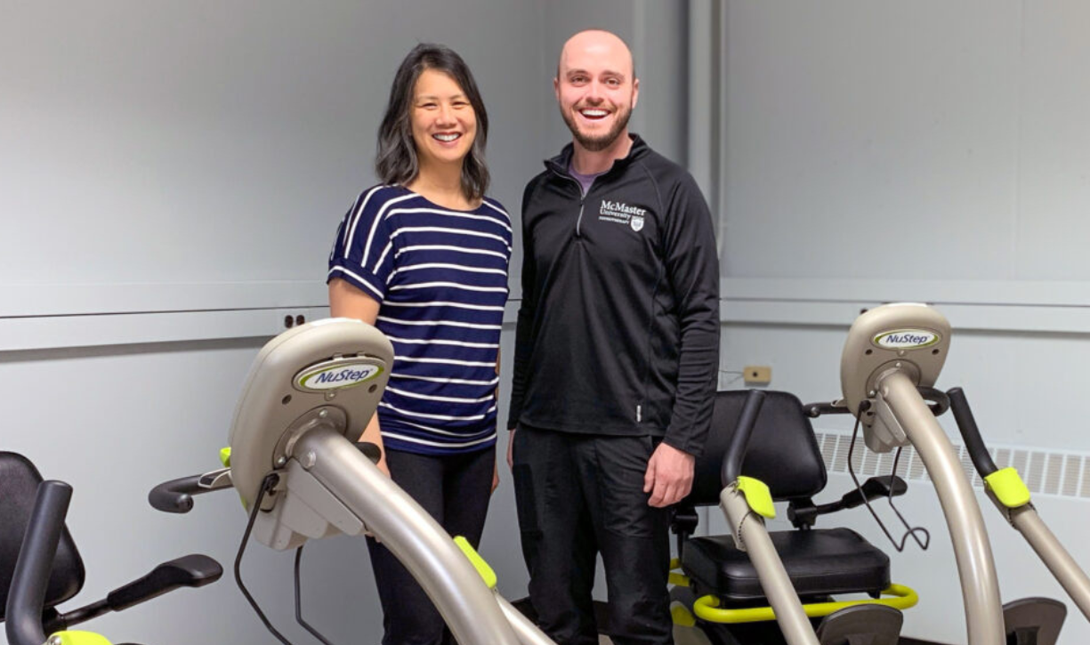 Ada Tang and Kevin Moncion stand together smiling in a room with multiple exercise bikes.