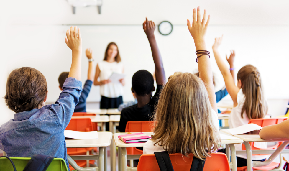 Several students raise their hands while seated in a classroom.