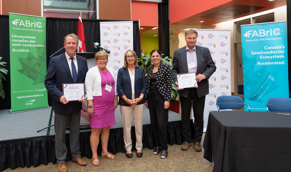 Five people standing posing for a photo. Two of them are holding certificates.