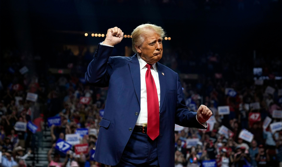 Donald Trump in a blue suit and red tie lifts his first in the air on stage.