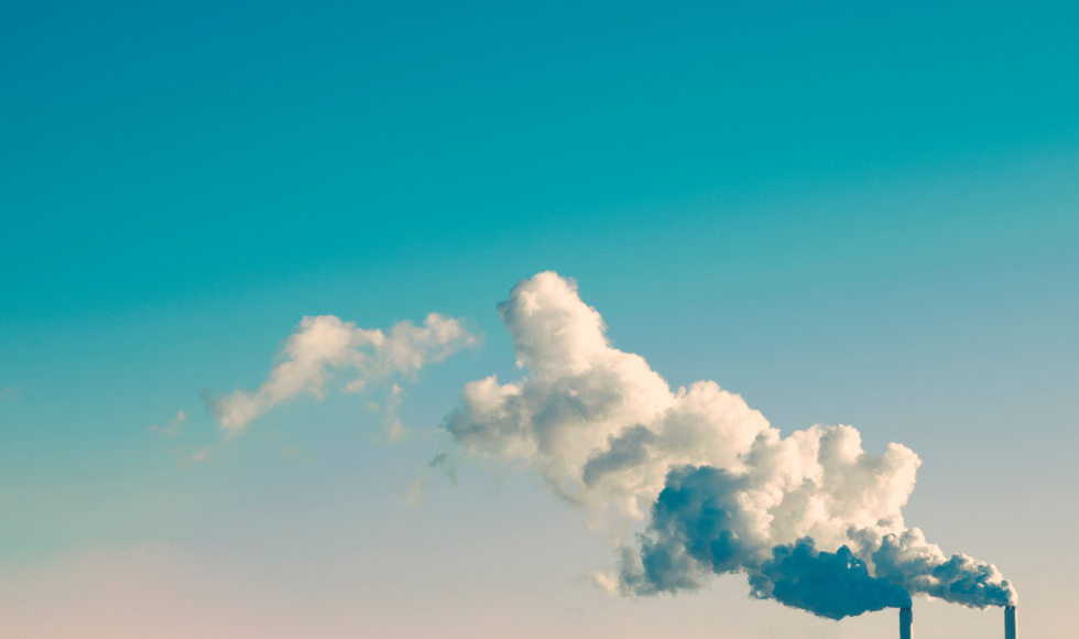 Billowing smoke coming from two smoke stacks against a blue sky