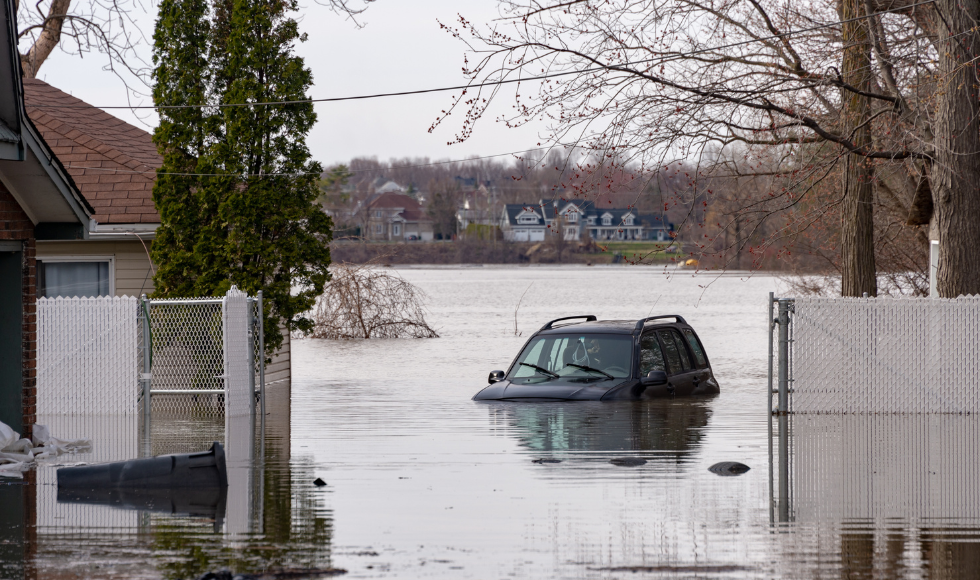 A heavily flooded residential area. A vehicle can be seen floating in a large body of water with houses nearby.