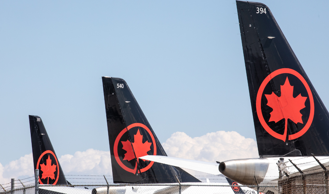 The tails of three planes with Air Canada's maple leaf branding on them, waiting side by side on the tarmac on a sunny day.