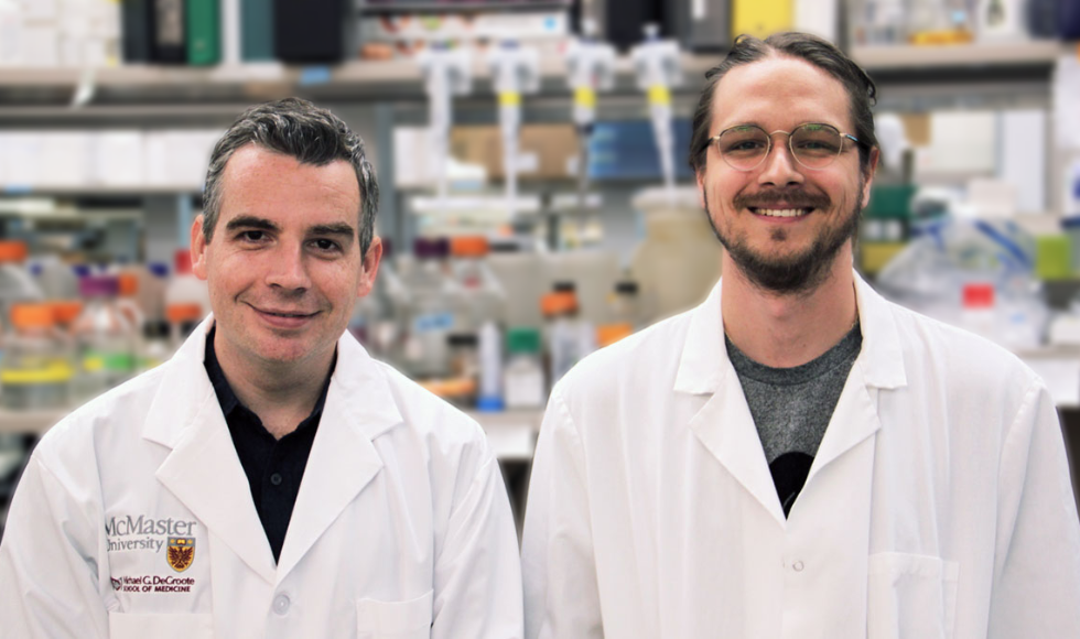 Two smiling adults wearing lab coats, in a McMaster lab.