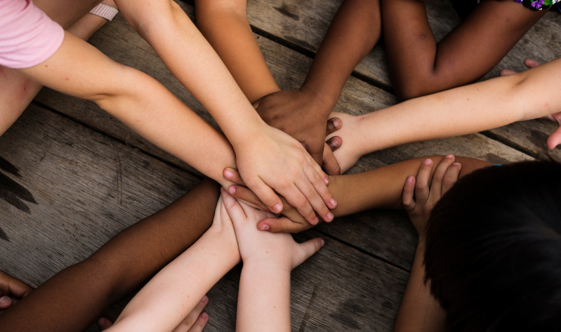 Seen from above: A circle of children's arms, with their hands clasped.