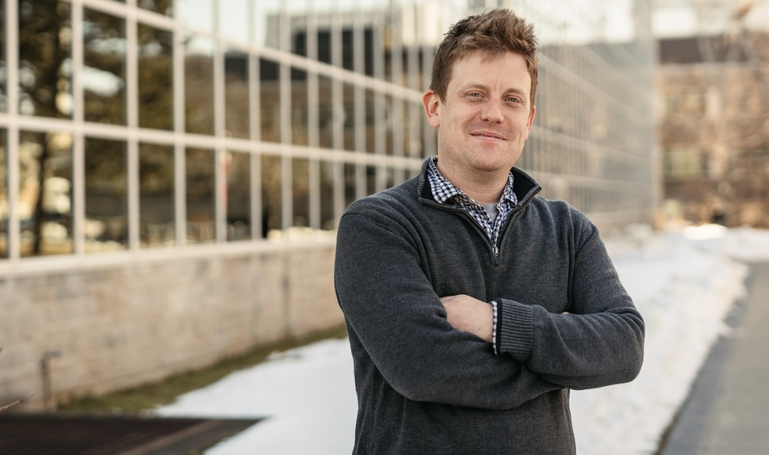 Andrew Gadsden smiling with his arms crossed standing outside the Engineering building on a cold day.