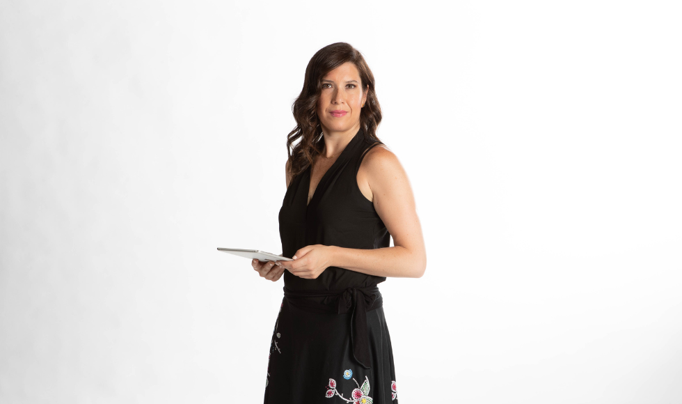 Chelsea Gabel standing against a white backdrop while holding a iPad and looking directly at the camera.