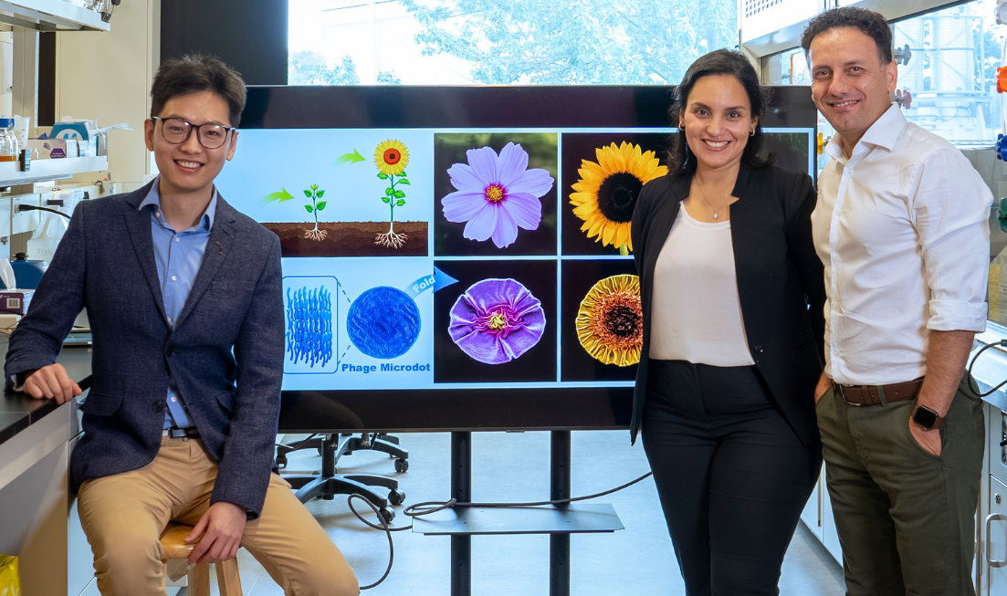 Three smiling people in a lab flank a screen showing the images of viruses and the flowers they resemble