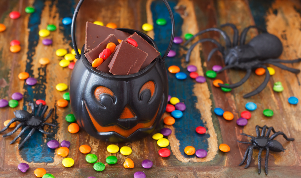 a plastic jack-o-lantern full of chocolate, surrounded by little colourful chocolates and plastic spiders.