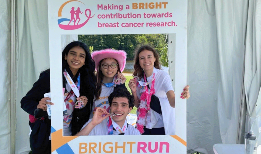 Four smiling students look through a big cardboard frame at the Bright Run event