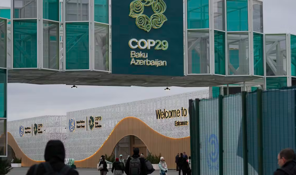 People walking into a building. On the side of the building are signs indicating it is a fathering spot for the COP29 summit in Baku, Azerbaijan.