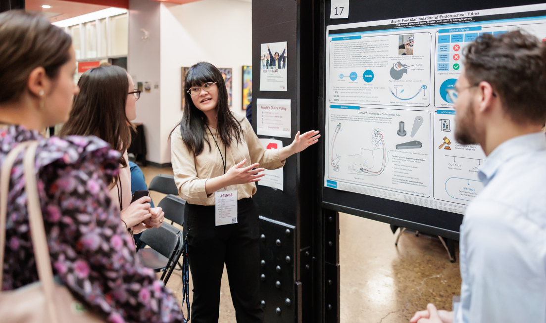 A person explains their poster presentation to 3 people at a previous Innovation Showcase.