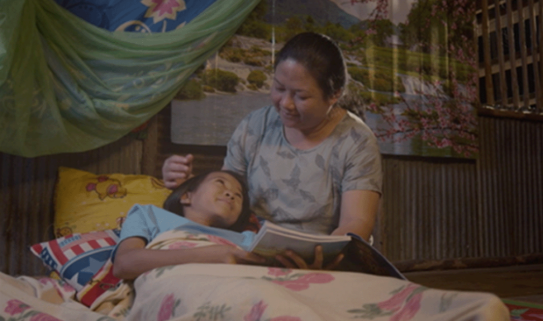 A scene from a film with a woman sitting beside a child in bed, stroking the child's head as both smile at each other.