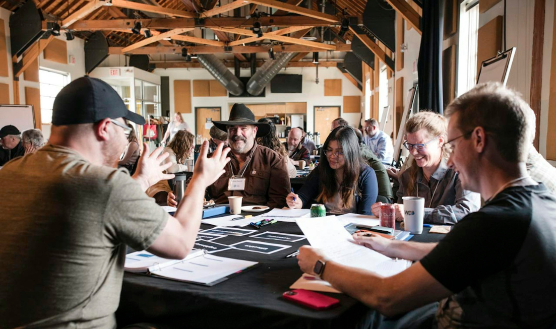 Groups of people sitting at tables and talking animatedly in a big room.