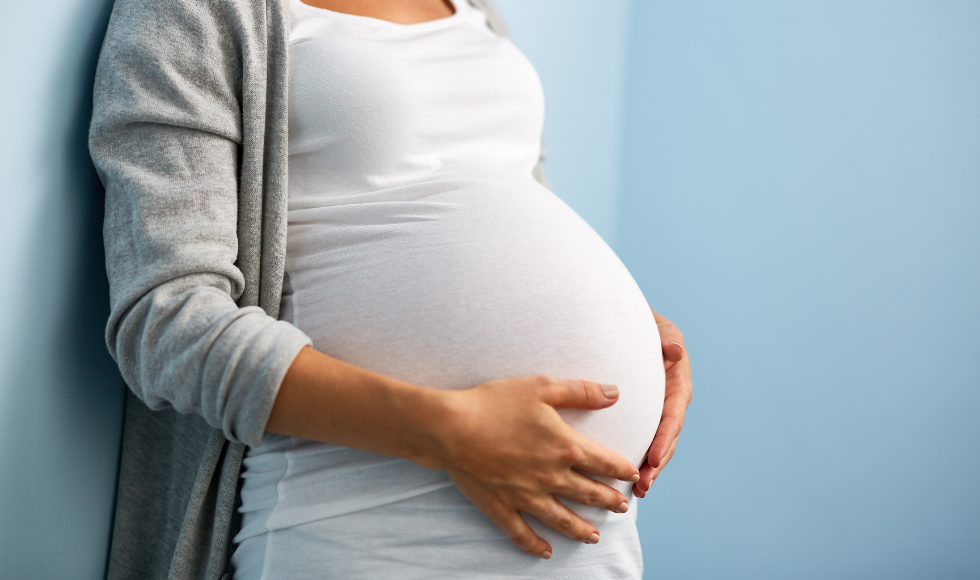 A pregnant woman stands with her hands cupping her stomach.