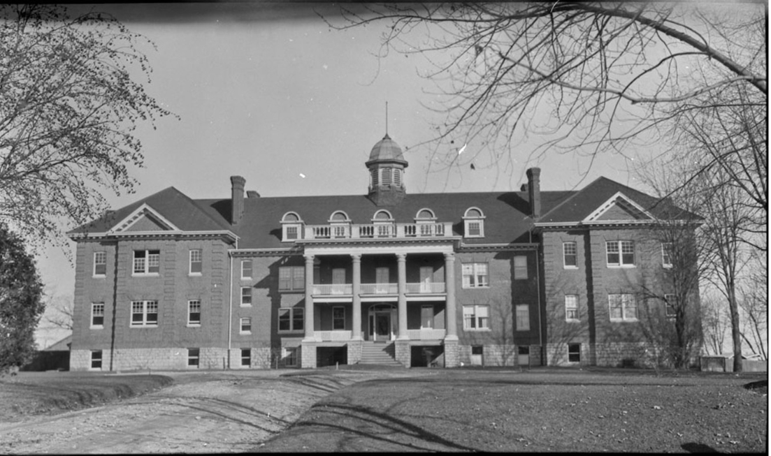 A black and white photo of a large brick building surrounded by trees