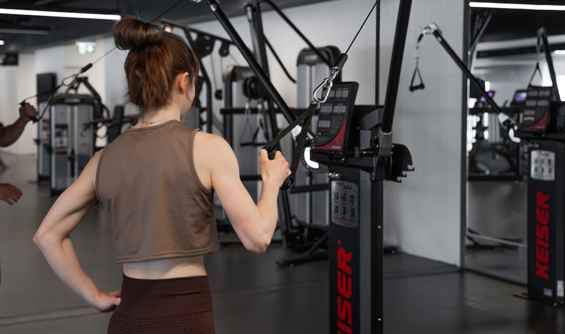 Seen from behind, a woman in exercise gear working with weight equipment in a gym.