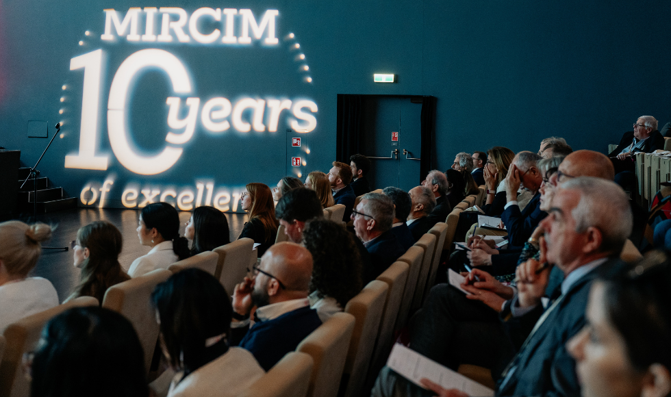 People sitting in theatre seats at a conference. On the wall the words