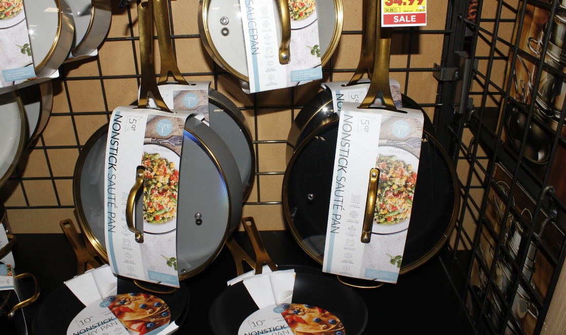 Non-stick pans for sale, hanging on hooks in a store display.