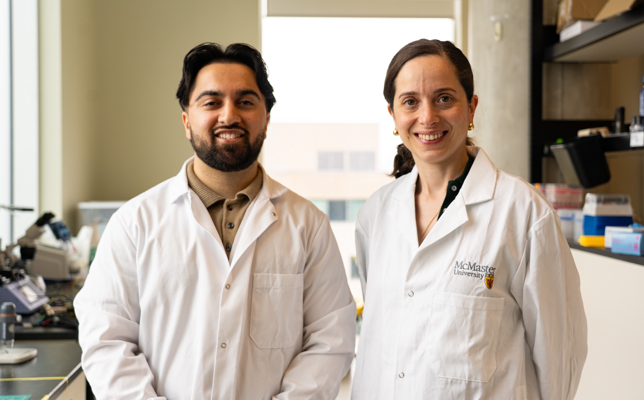Two people in lab coats smile, facing forward.