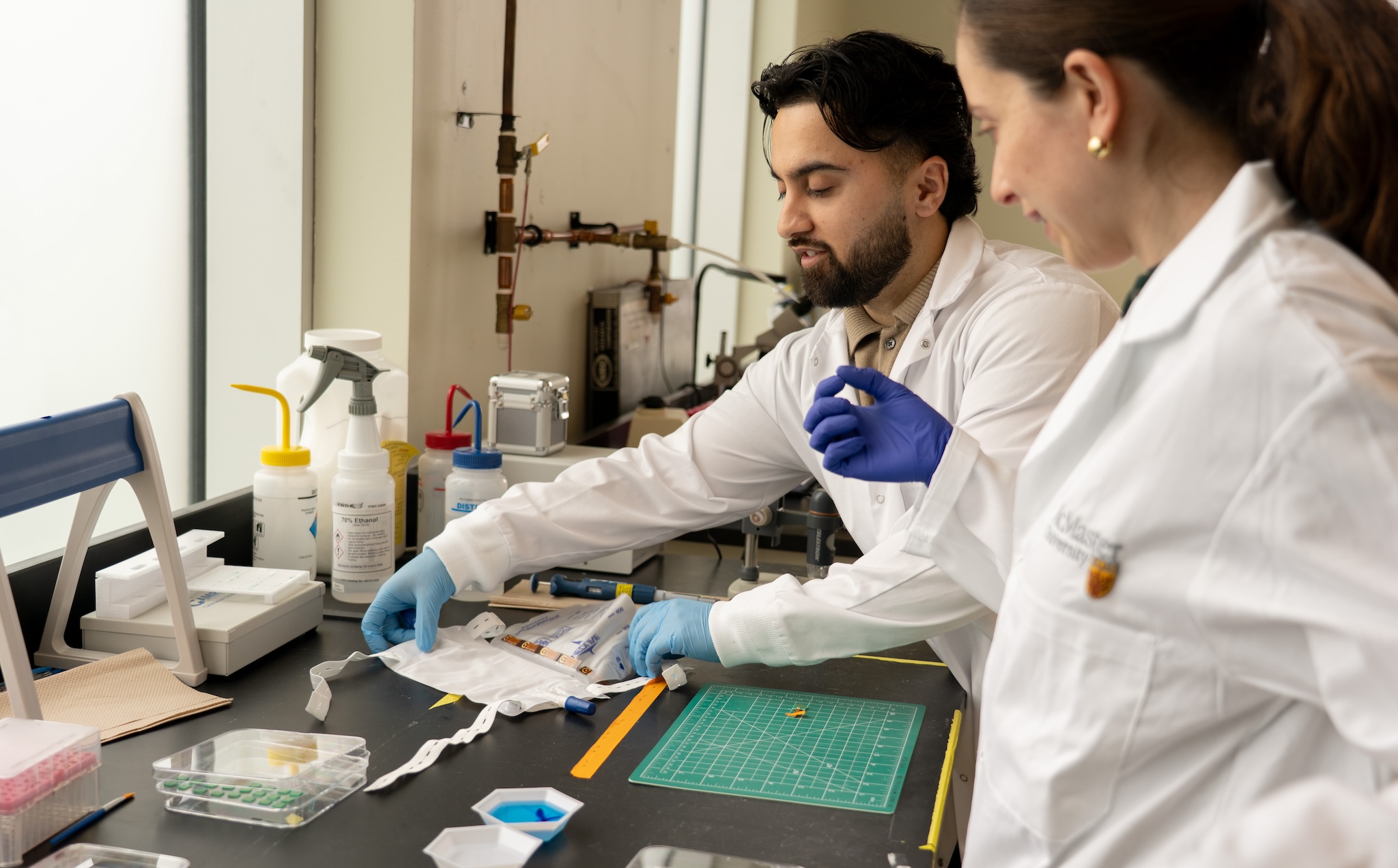 Two people in lab coats work at a lab bench.