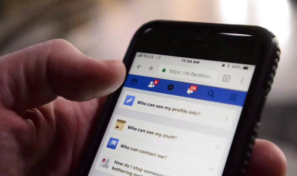 A person's hand holds a smart phone, which is open to show a Facebook page on privacy settings.