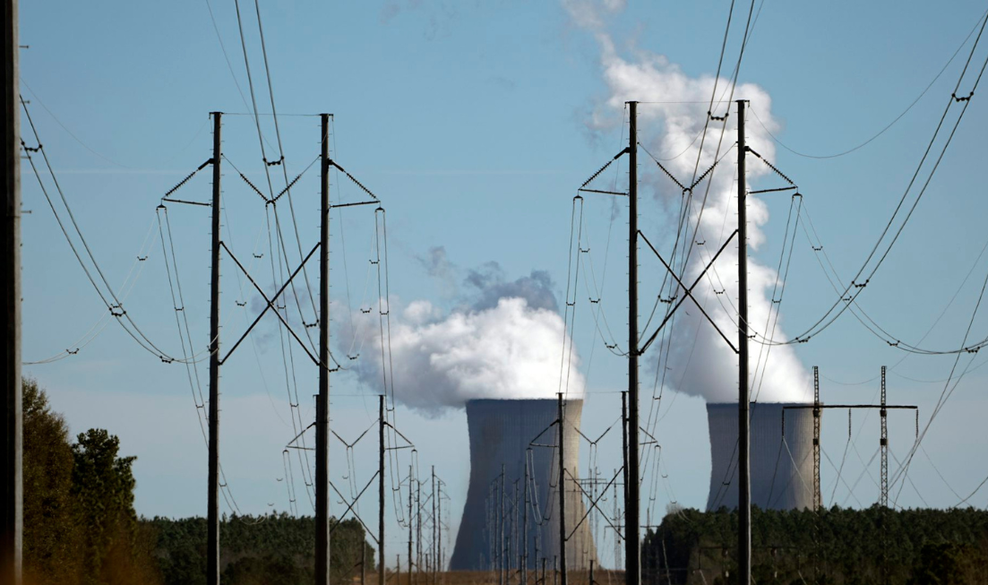 Thick columns of vapour pour from the openings of two nuclear power plant cooling towers, seen behind power lines.