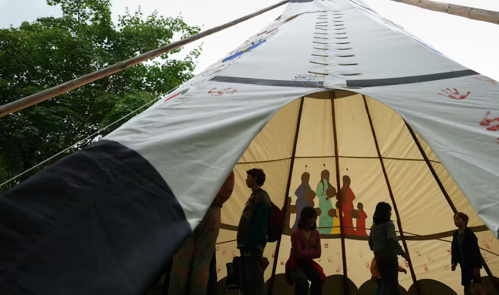 Students are silhouetted while standing inside a painted teepee.